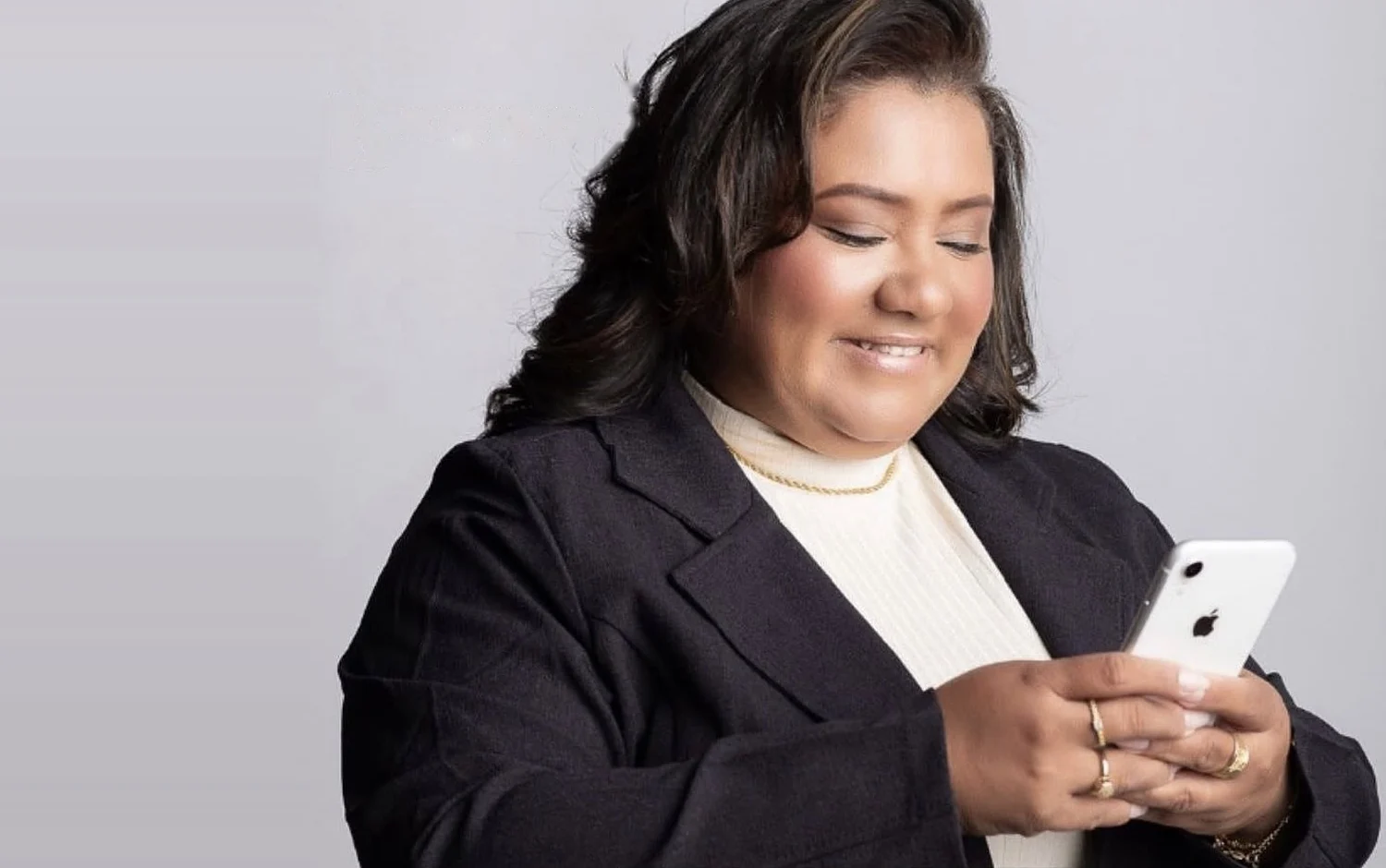 Rose Braga de blazer escuro, a sorrir enquanto olha para o telemóvel